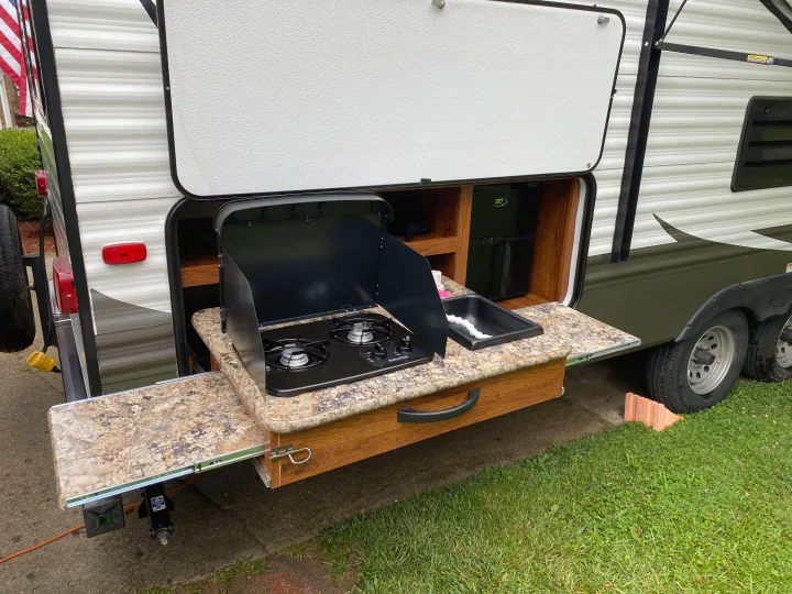 RV rental: Outdoor kitchen pulled out from an RV, featuring a two-burner stove, sink, and counter.. Keystone Hideout 2014