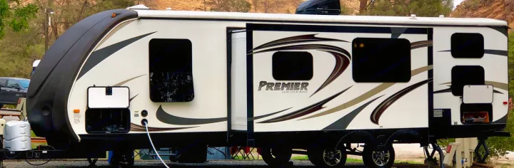 RV rental: A white and black Premier travel trailer, with its slide-out extended, is parked at a scenic campground.. Keystone RV Bullet Premier 2015