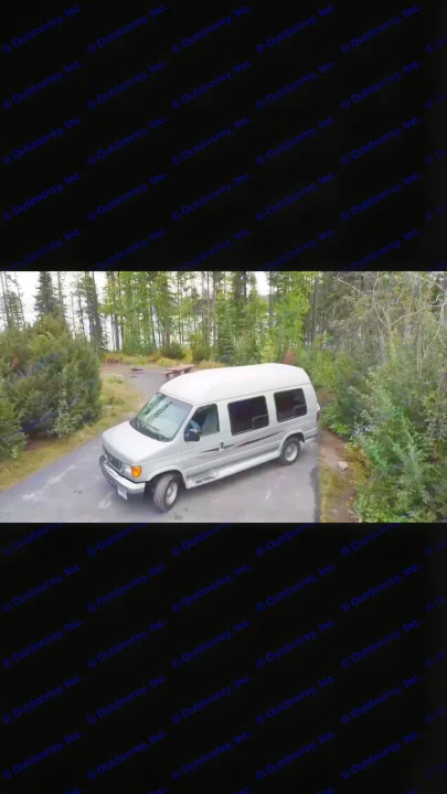 An RV rental silver van awaits adventure at a tranquil forest campsite with a lake in the background.. Ford Econoline 2006