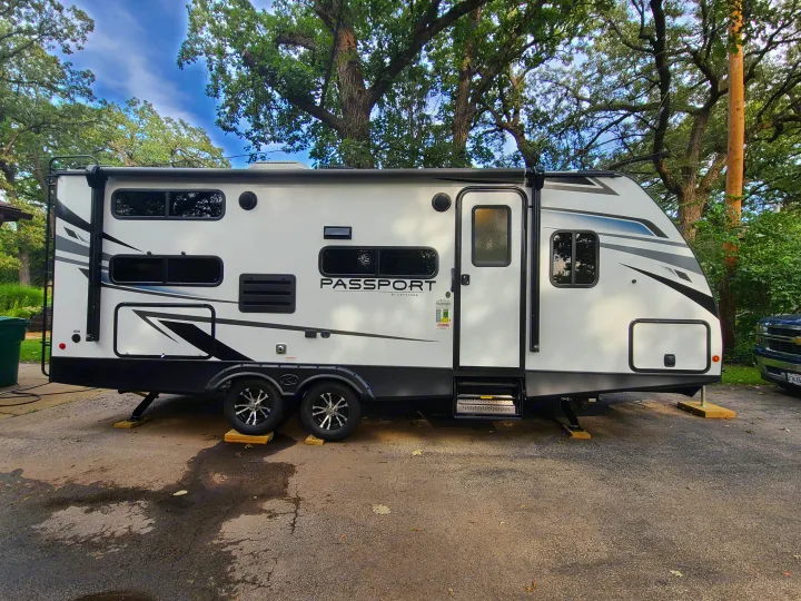 Modern white Keystone Passport travel trailer/RV, ideal for an rv rental, parked outdoors with green trees & blue sky.. Keystone Passport 2021
