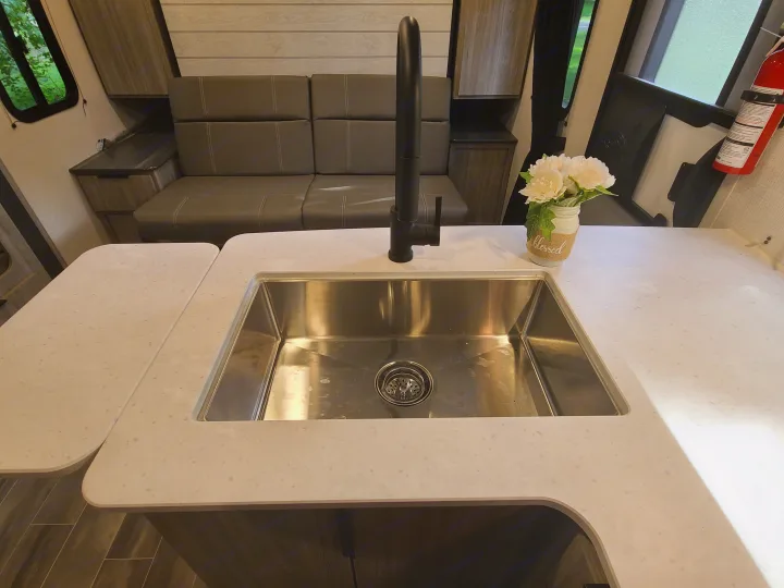 Spacious rv rental interior featuring a modern kitchen with a large stainless steel sink, sleek faucet, and comfortable sofa.. Keystone Passport 2021