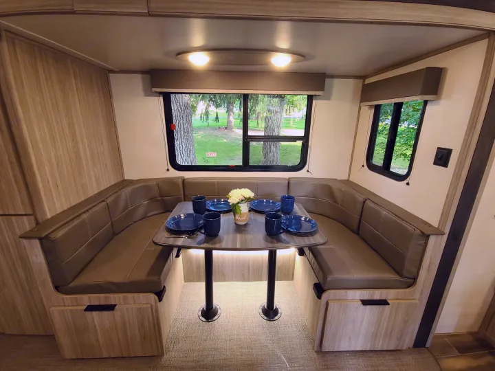 Spacious RV rental dinette: U-shaped seating, set table with decor, and large windows showing trees outside.. Keystone Passport 2021