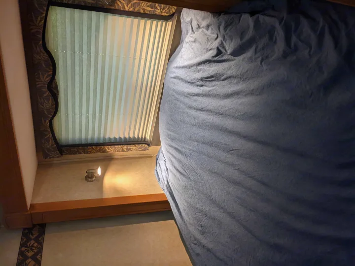An RV rental bedroom with a blue bed, pleated window blinds, and a wall-mounted light.. Forest River Lexington 2008