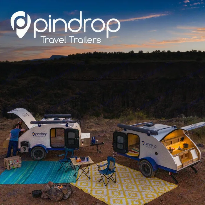 Pindrop RV rental: Two modern teardrop campers with outdoor rugs, tables, and a campfire set up at dusk.. Pin Drop Travel Trailers Scout 2022