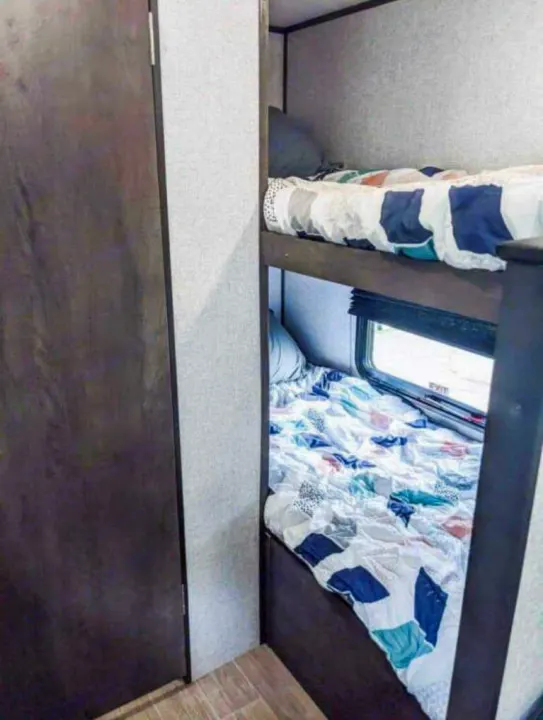 An RV rental's sleeping area: practical bunk beds with patterned bedding and a window for the lower bunk.. Coleman Other 2021