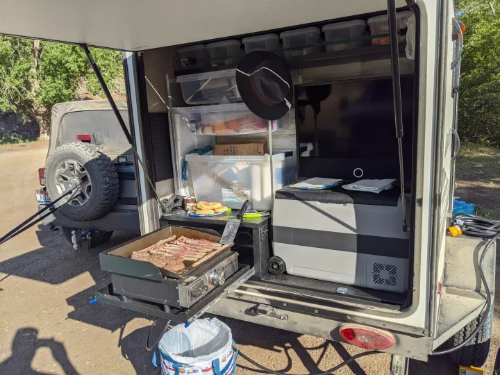 RV rental outdoor kitchen with a Blackstone griddle cooking bacon, storage, and portable fridge, perfect for camping meals.. Jayco Jay Feather Micro 12SRK 2021