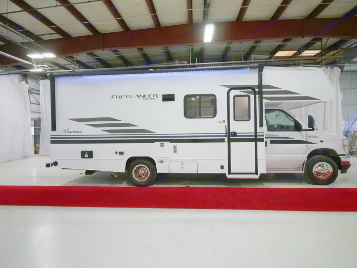 Side view of a white Coachmen Freelander Class C motorhome for RV rental, with black and blue graphics, and bright awning lights.. Coachmen Freelander 23FS 2022
