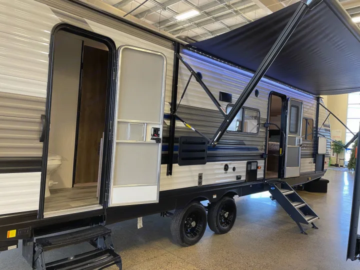 Large travel trailer, perfect for RV rental, with open doors showcasing interior. Lit awning and steps extended.. Pioneer 27fqs 2021