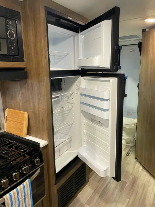 Efficient RV rental interior showcasing a compact kitchen with an open fridge and a peek into the bathroom.. Pioneer 27fqs 2021