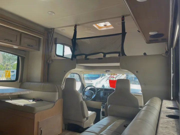 Spacious RV rental interior featuring a cozy dinette, overhead bunk with safety net, and driver's cockpit.. Thor Four Winds 2021