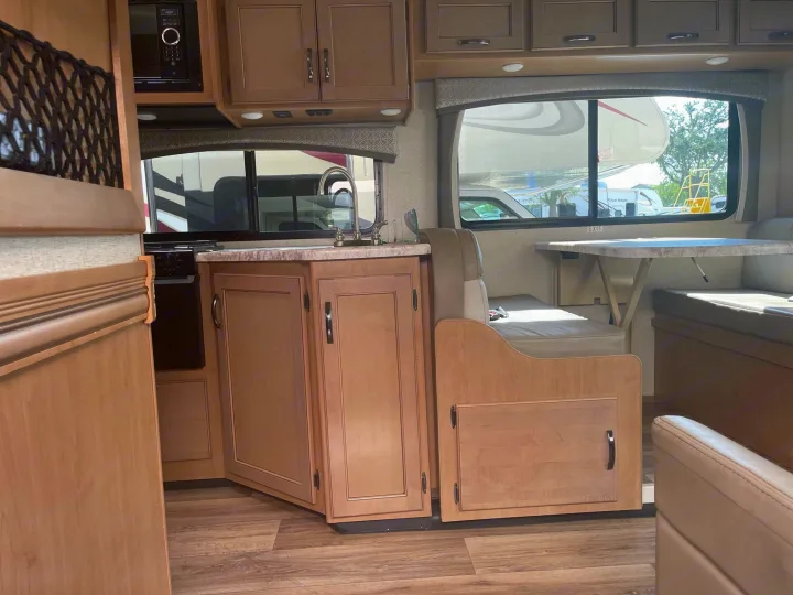 RV rental interior: kitchen with sink, microwave, dinette, and light wood cabinetry over wood-look floors.. Thor Four Winds 2021