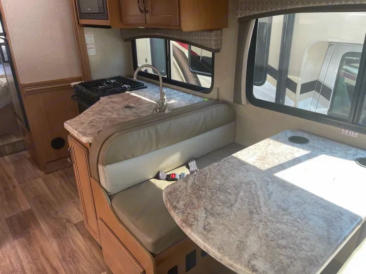 RV rental interior: a compact kitchen with a stove & sink, plus a dinette with table and seatbelts for travel.. Thor Four Winds 2021