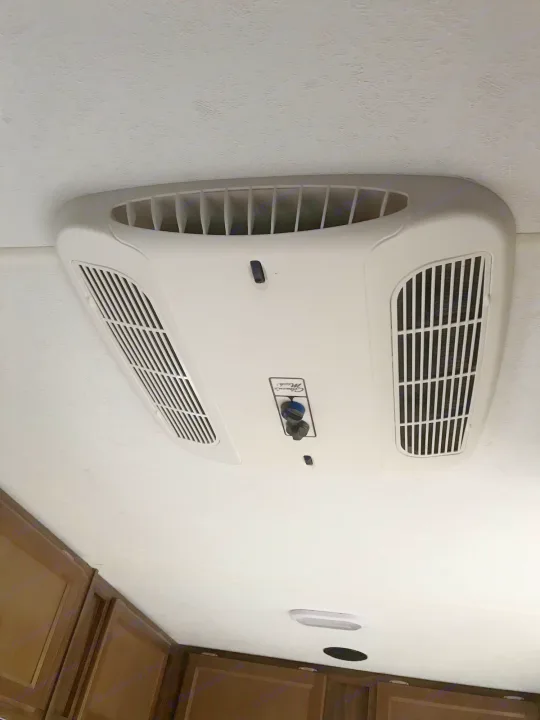 RV rental interior featuring a white ceiling-mounted RV air conditioner with vents and controls, above brown cabinets.. Coachmen Clipper 2016