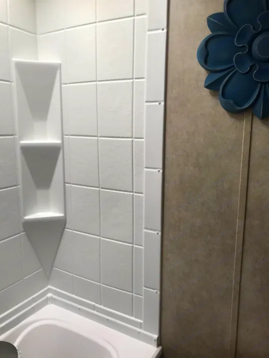 RV rental bathroom: compact white shower walls with built-in shelves, and a decorative blue flower accent.. Coachmen Clipper 2016