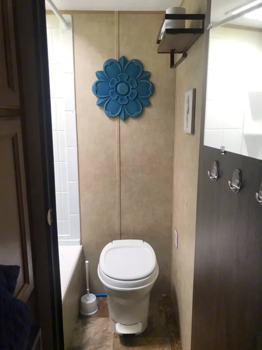 RV rental bathroom: compact design with white toilet, shower, blue floral decor, and hooks on door.. Coachmen Clipper 2016