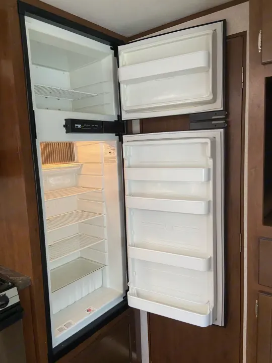 Empty RV rental refrigerator and freezer with open doors, showing clean interior shelves. Ideal for your next trip.. Jayco Jay Flight 2017