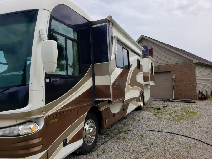 This large brown & white Revolution motorhome, an RV rental with extended slide-outs, is parked on a gravel driveway.. Fleetwood Revolution 2002