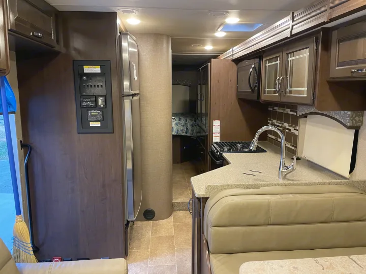 Spacious RV rental interior: modern kitchen with stainless appliances, dinette seating, and sleeping area. Control panel and broom near entrance.. Thor Motor Coach Chateau 2017