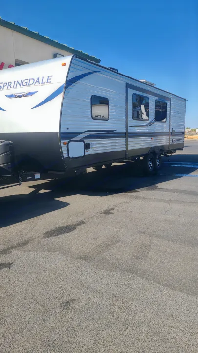 A large, light grey and white Springdale travel trailer RV, perfect for an RV rental, parked on asphalt.. Keystone Springdale 2022