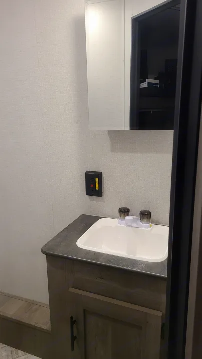 This RV rental features a compact bathroom vanity with a sink, faucet, medicine cabinet, and outlet.. Keystone Springdale 2022