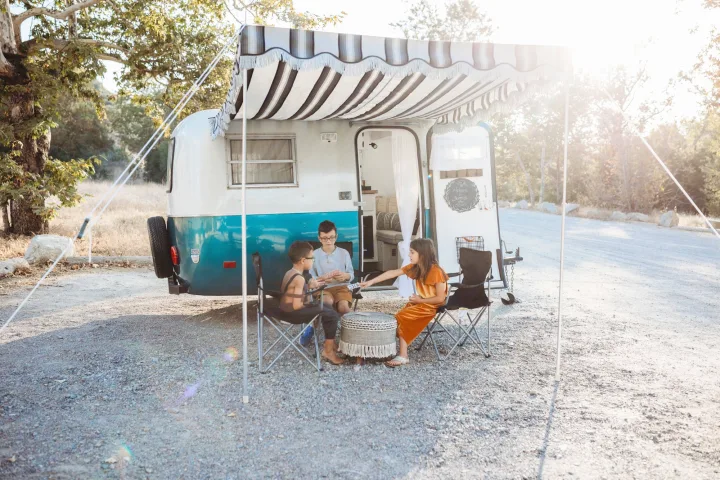 Three kids enjoy a family camping trip, playing cards outside their charming vintage RV rental with an extended awning.. Scamp 13' 1979