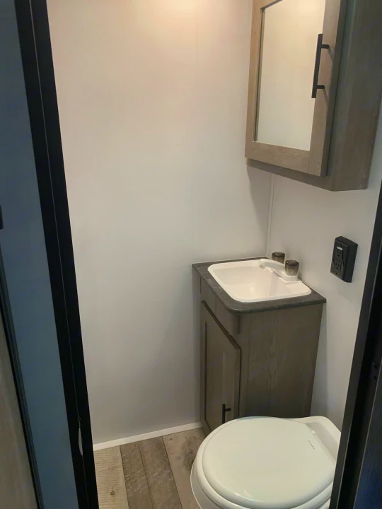 RV rental bathroom: Compact toilet, sink, vanity, and mirrored cabinet offer essential amenities for travel comfort.. Keystone Springdale 2021
