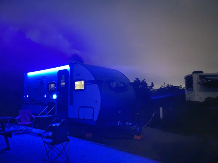 Nighttime rv rental setup: a travel trailer at a campsite, illuminated by cool blue lights, with chairs ready for stargazing.. Forest River Cherokee Wolf Pup Black Label 2021