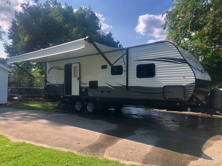 Spacious white and gray travel trailer with extended awning, ideal for your next RV rental. Parked on a sunny day.. Jayco Highland Ridge 2019
