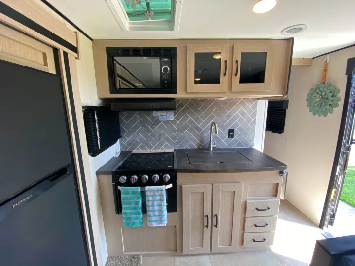 Explore this clean, modern RV rental kitchen: fridge, microwave, stove, sink, light cabinetry, and trendy herringbone backsplash.. Coachmen Other 2021