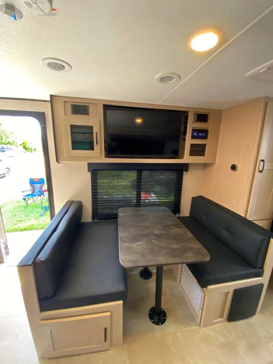 Spacious RV rental interior featuring a dinette with black benches, table, and an overhead entertainment center with TV.. Coachmen Other 2021