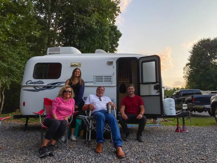 Four happy people relaxing outside their white Casita RV rental on a gravel campsite. Enjoying their camping trip!. Casita 17' Spirit Deluxe 2010
