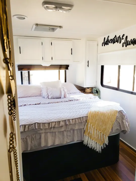 Cozy RV rental bedroom featuring soft lavender bedding, a bright yellow throw, and "Adventure Awaits" decor.. Coachmen Freelander 2014