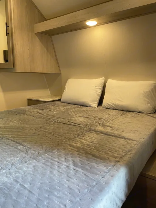 Interior of an RV rental: a compact bedroom with a bed, two white pillows, and warm accent lighting.. Dutchmen Coleman 2022