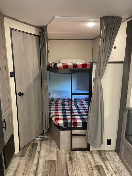 Inside an RV rental: two compact bunk beds with plaid blankets & privacy curtains, ideal for family sleeping.. Dutchmen Coleman 2022