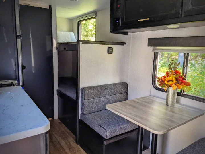 Cozy RV rental interior with light walls and dark trim, featuring a dinette, bunk beds, and a compact kitchen.. Forest River Cherokee Wolf Pup 2021