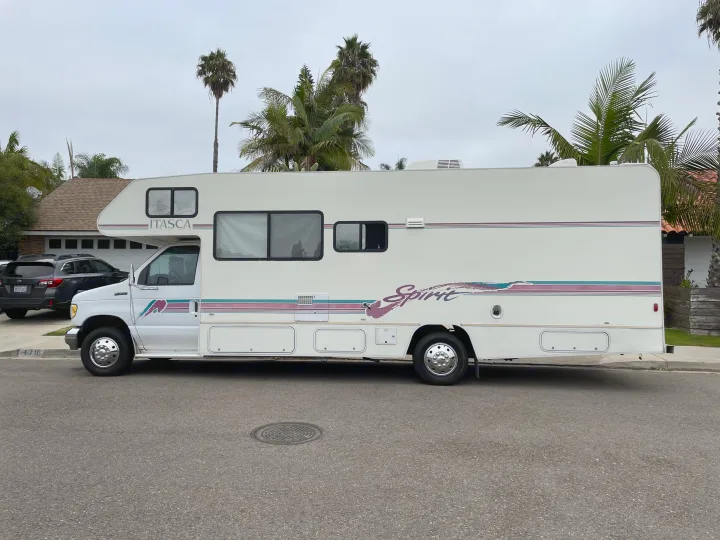 White Itasca Spirit RV rental parked on a residential street, with palm trees and a house in the background.. Itasca Spirit 1995