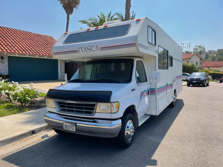 White Winnebago Itasca RV rental parked curbside on a sunny residential street.. Itasca Spirit 1995