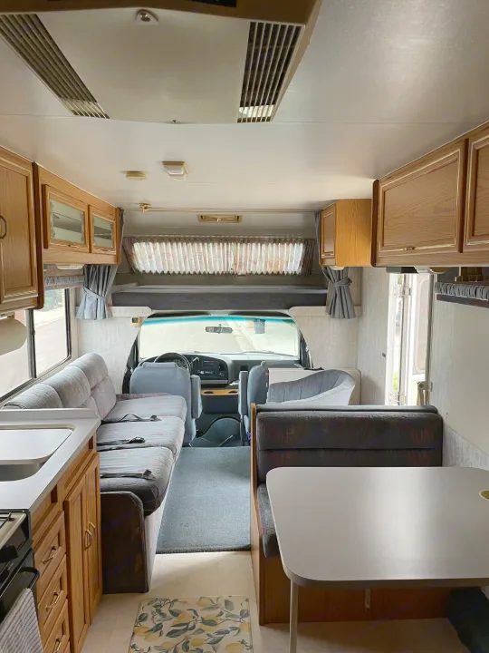 Spacious RV rental interior with kitchen, dining, and sleeping areas, leading to the driver's cabin and overhead bunk.. Itasca Spirit 1995