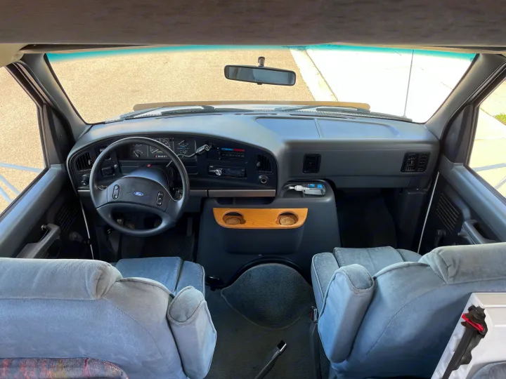 Inside this RV rental: Dashboard, steering wheel, and light blue front seats, offering a clear view out the windshield.. Itasca Spirit 1995