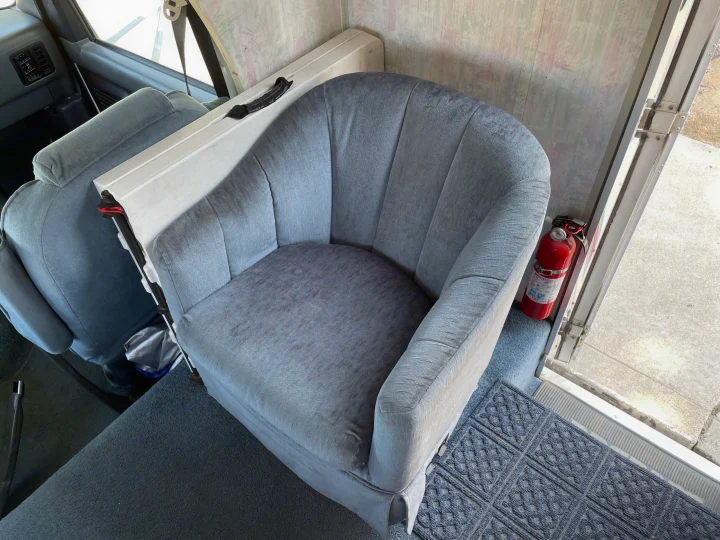 RV rental interior: a comfy grey armchair, essential fire extinguisher, and patterned floor mat by the door.. Itasca Spirit 1995