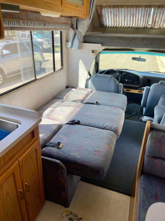 This rv rental's interior reveals multi-functional seating with seatbelts, a small kitchen, and driver's area, perfect for travel.. Itasca Spirit 1995