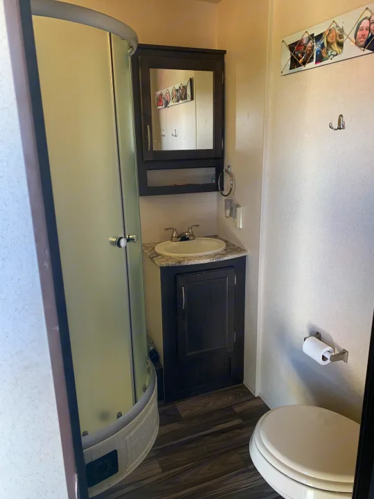 Compact RV rental bathroom featuring a curved shower, vanity with sink, and toilet.. Forest River Stealth 2018