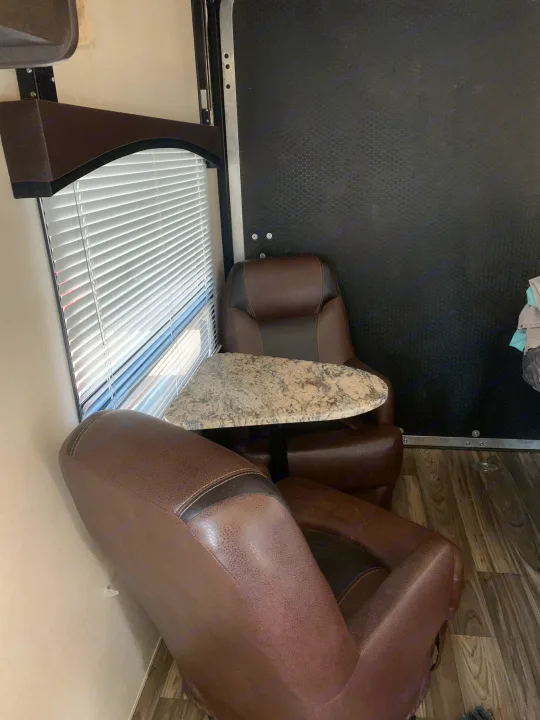 RV rental's cozy dinette: two brown recliners & a small triangular table by a window with blinds.. Forest River Stealth 2018