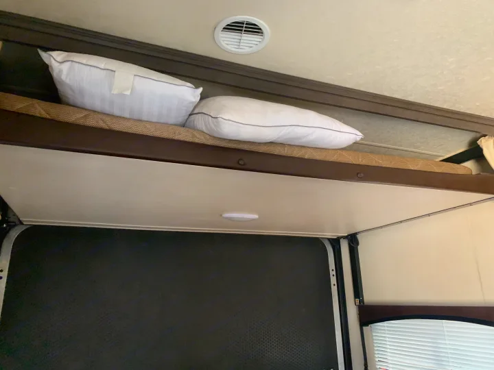 RV rental interior: Elevated bunk with pillows, a ceiling vent, and a durable, dark textured floor below.. Forest River Stealth 2018