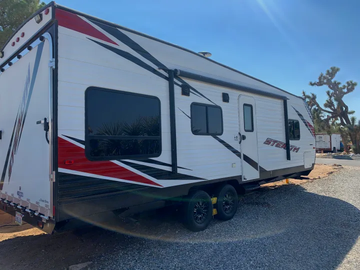 This white Stealth travel trailer RV rental is parked on a gravel lot, ready for your desert adventure.. Forest River Stealth 2018