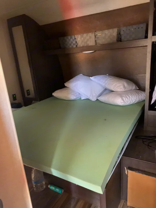 Compact RV rental sleeping area with green foam mattress, white pillows, and overhead storage.. Forest River Stealth 2018