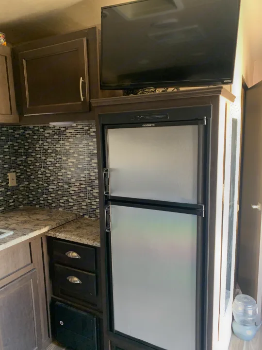 Inside this RV rental: A kitchen with a Dometic refrigerator, Vizio TV, dark wood cabinets, and tiled backsplash.. Forest River Stealth 2018