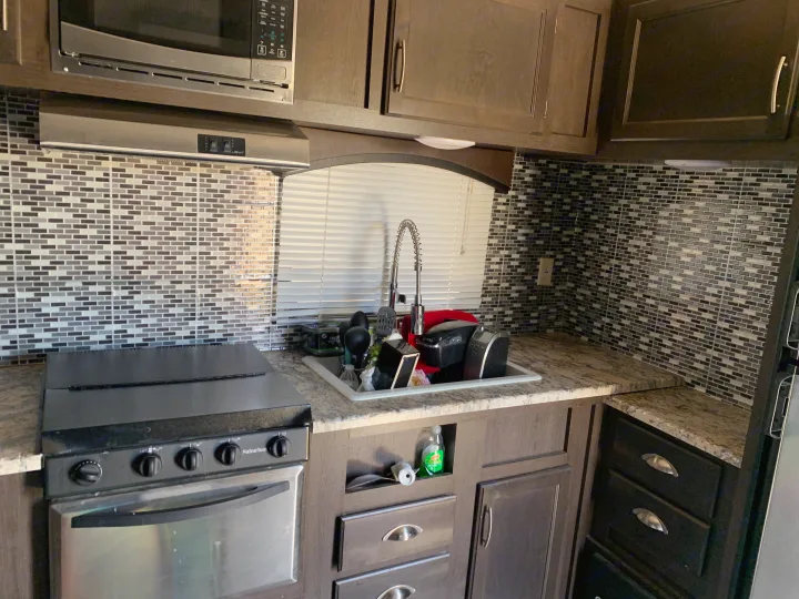 RV rental kitchen: Compact with microwave, stove, and sink. Dark cabinets, granite-look counters, and mosaic tile backsplash are visible.. Forest River Stealth 2018