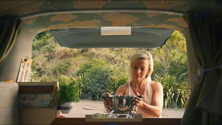 Woman preparing a meal in a cozy **rv rental** camper van, showcasing portable kitchen convenience and outdoor living.. Toyota Noah 2005