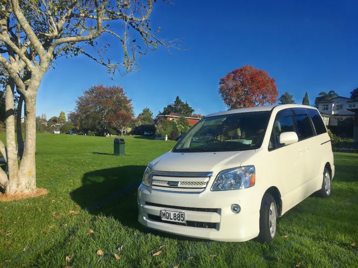 White minivan parked on a sunny lawn. Ideal for travel or as a compact RV rental option.. Toyota Noah 2005